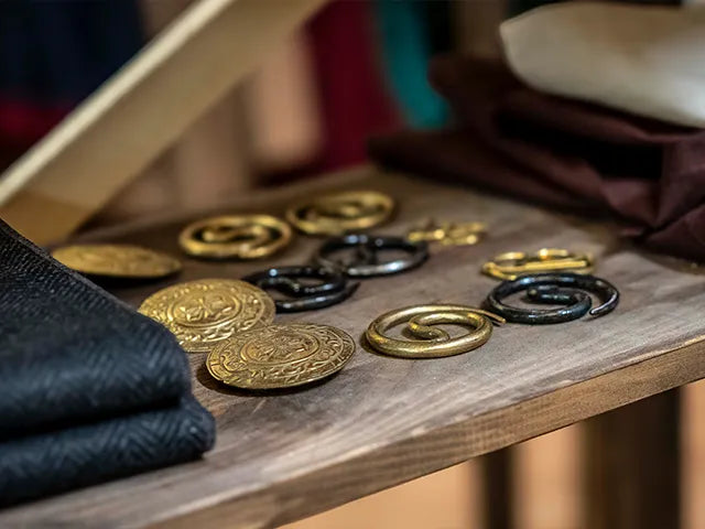Collection of gold and black circular metal broches and coins on a wooden surface