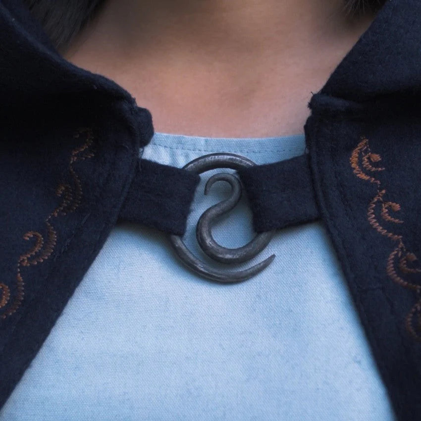 Close-up of a dark blue coat with decorative broche, worn over a light blue shirt.