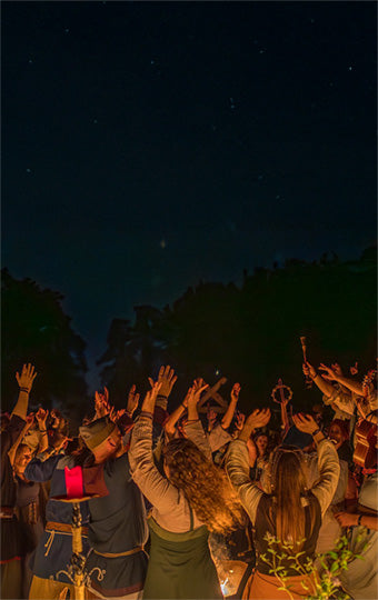 People gathered outdoors at night, raising their hands towards the sky.