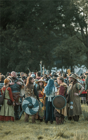 Group of people in historical or fantasy larp costumes standing in a field with trees in the background.