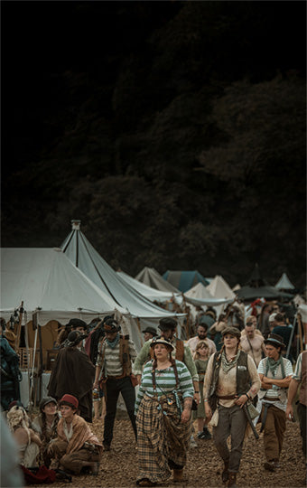 Group of people in medieval clothing at a larp festival with tents and trees in the background.