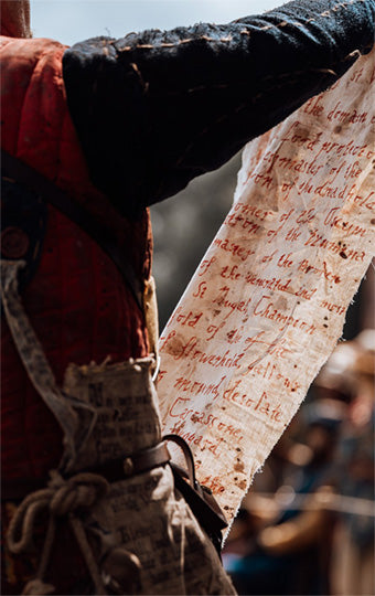 Person holding a tattered piece of paper with text, possibly historical or legal, against a blurred background.