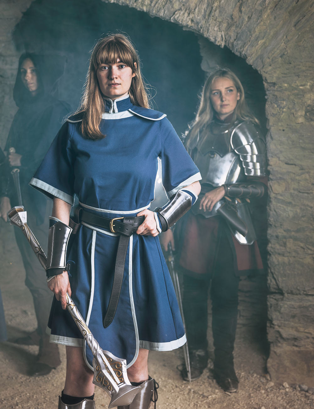 Person in blue medieval D&D outfit with armor, standing in a stone tunnel with other similarly dressed individuals.
