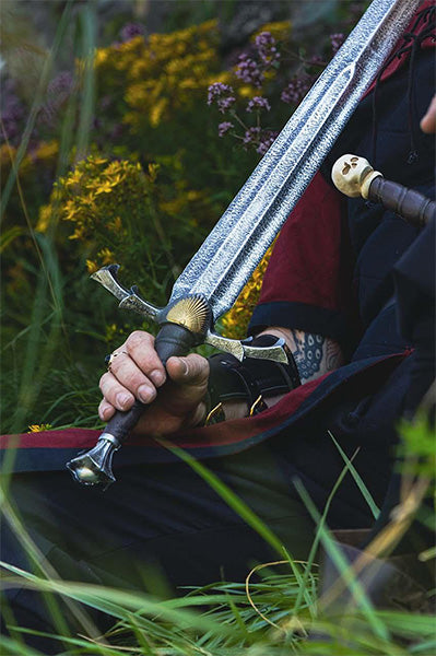 Person holding a dungeons and dragons LARP foam sword in a natural setting with greenery