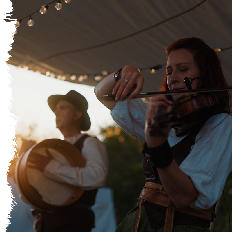 Two musicians playing instruments under a tent with string lights.