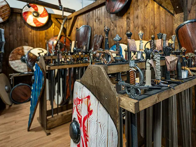 Display of medieval Larp items including swords, shields, and helmets in a wooden room.