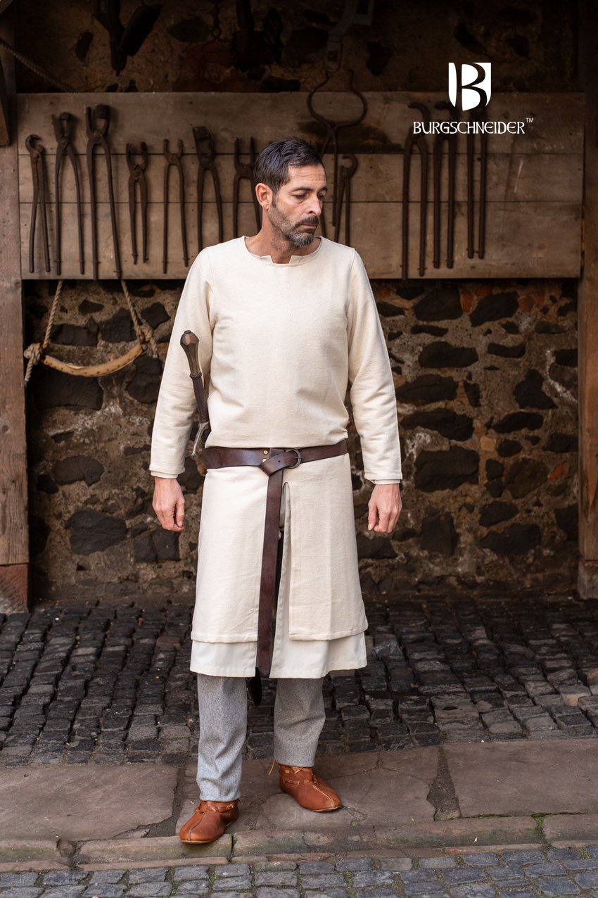 Man wearing a historical  tunic outfit with a sword in front of a stone wall with tools