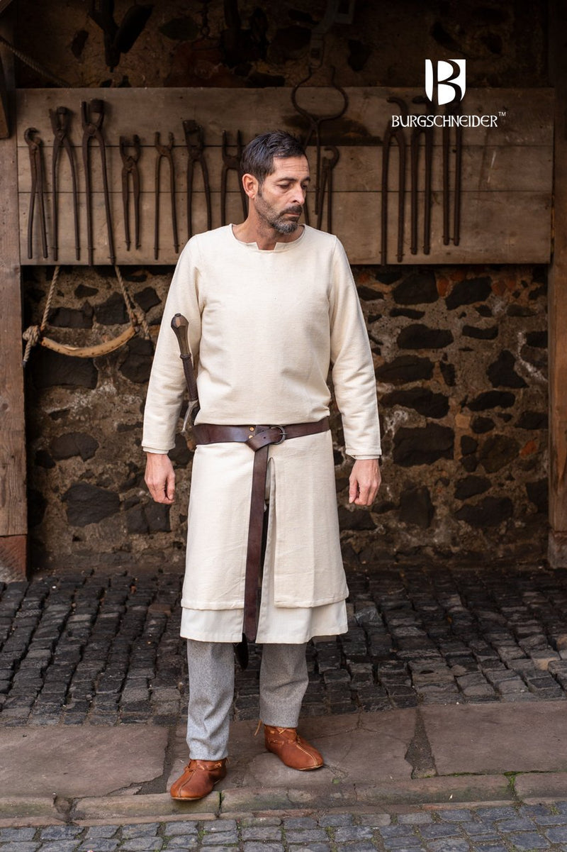 Man wearing a historical  tunic outfit with a sword in front of a stone wall with tools