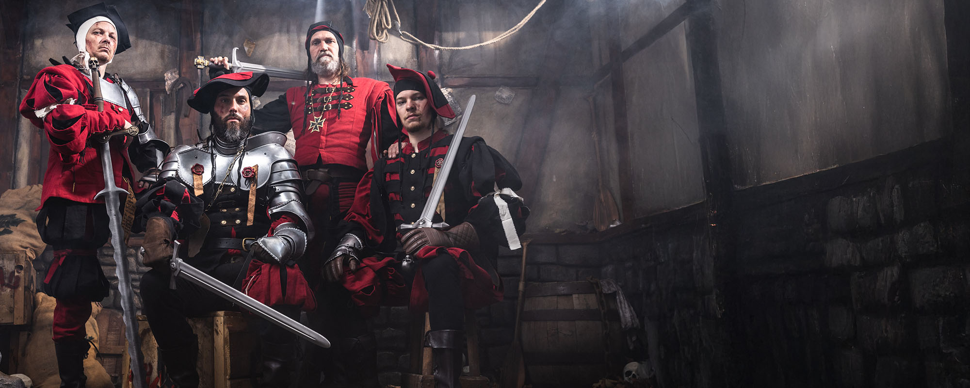 Four characters in medieval fantasy warhammer attire with swords in a dimly lit room.